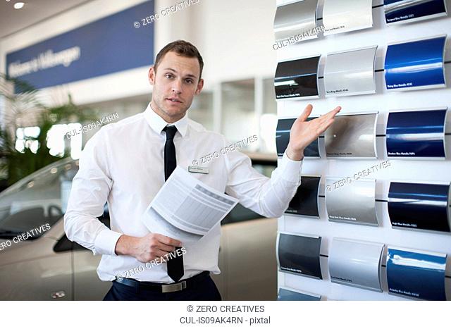 Portrait of salesman gesturing to color swatches in car dealership