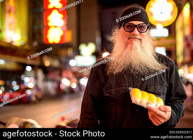 Portrait of mature handsome bearded tourist man exploring Chinatown in Bangkok city at night