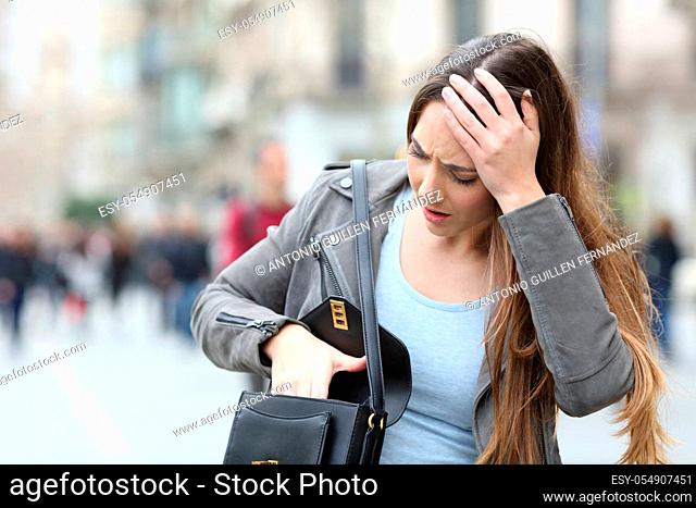 Front view of a worried woman looking preoccupied inside her bag on a city street