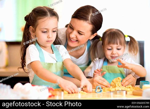 Mom with her little kids daughters are cooking holiday pie in the kitchen