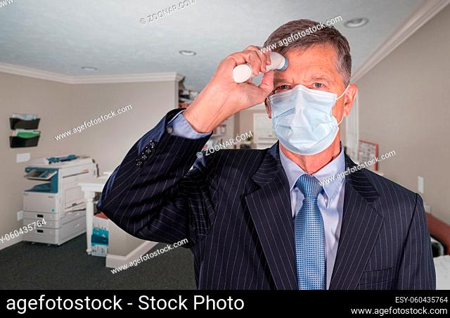 Mockup of senior adult wearing mask checking for a coronavirus fever with thermometer before going into office for meeting