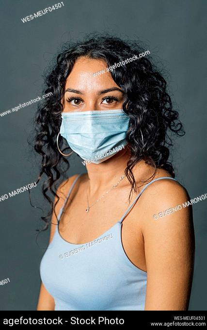Woman with curly hair wearing protective face mask against gray background