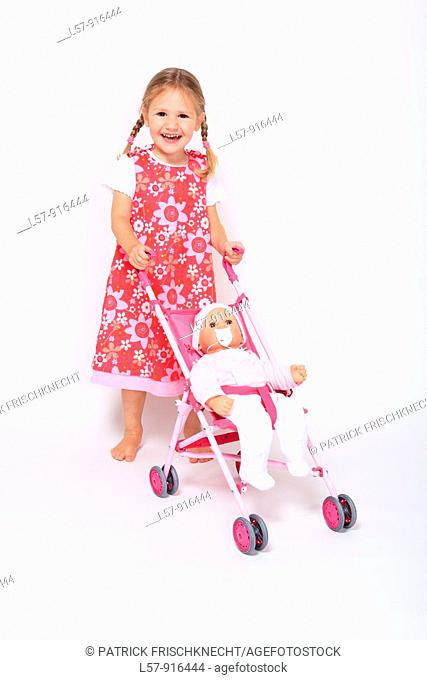little girl wearing dress standing with buggy pram and baby doll, white background, studio, Switzerland