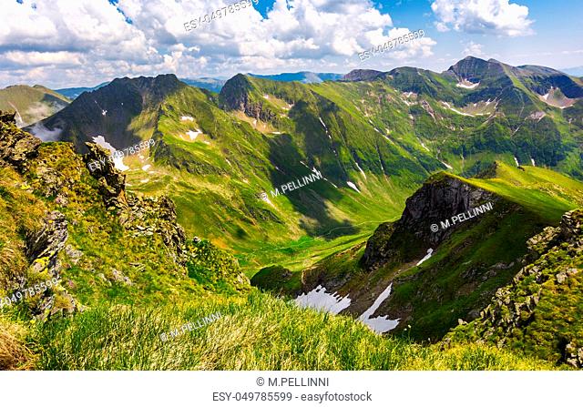 valley with snow in summer mountains. gorgeous mountainous landscape of Carpathians. rocky cliffs and grassy hillsides under a cloudy sky