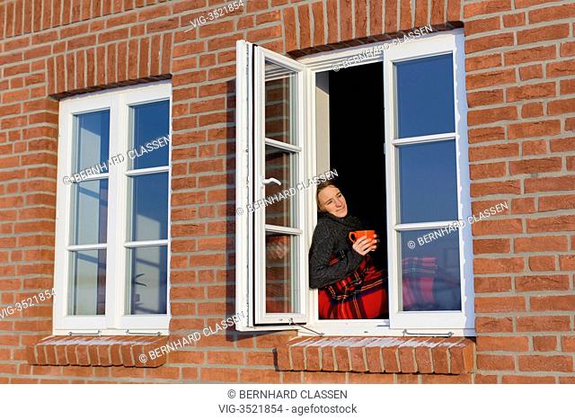 GERMANY, BARNSTEDT, 23.01.2013, Young woman, 35 years, sitting in the winter with a warm drink and a blanket in a window