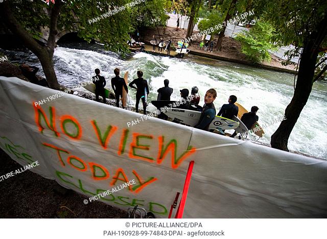 28 September 2019, Bavaria, Munich: Surfers stand on the area of the Eisbachwelle, which is closed off with a screen. One of the privacy fences says ""No View...