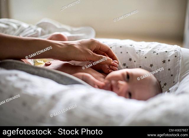 Mother touching innocent newborn baby boy in bassinet