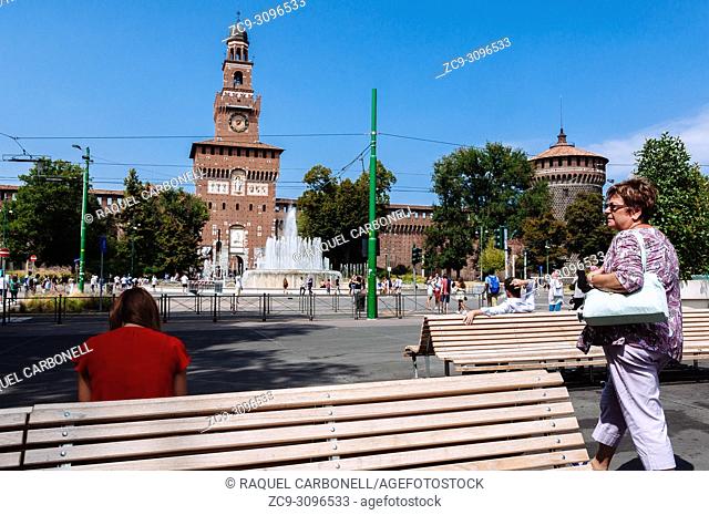 People sit on public benches looking to Piazza Castello square fountain with the Torre del Filarete in Sforza Castle at back, Milan, Lombardy, Italy