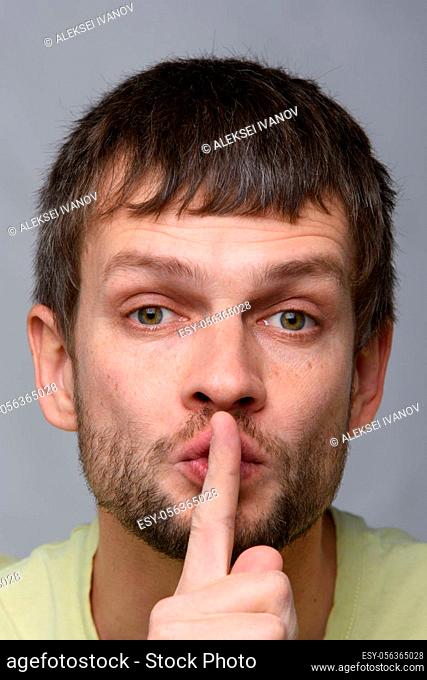 Portrait of a man of European appearance who put a finger to his mouth, gesture of silence, close-up