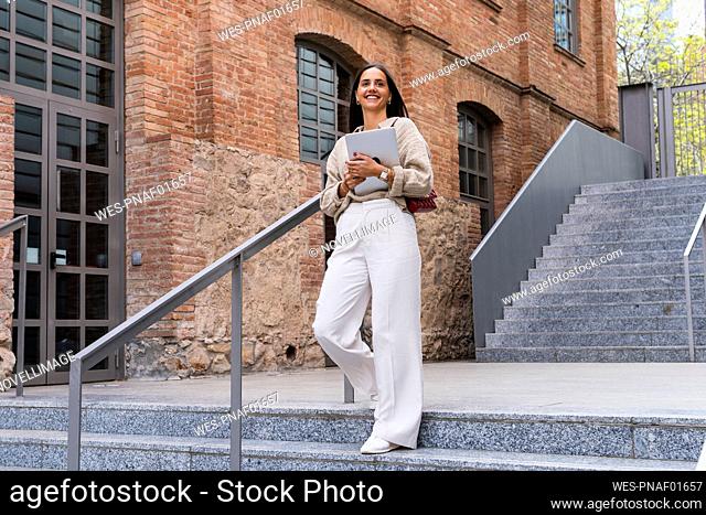 Smiling woman with laptop moving down from steps