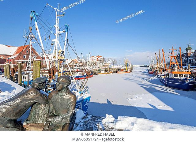 Winter atmosphere, fishing monument, old and young fishermen with shrimp boat in the harbour of Neuharlingersiel, Eastern Frisia, Lower Saxony, Germany