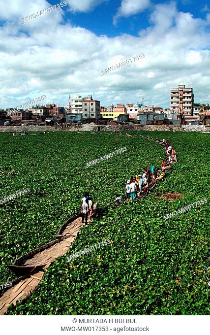 People are crossing a canal through a boat-bridge, near Kamrangir Char, in Lalbagh area of Old Dhaka Usually boatmen ferry the passengers by their boats But...