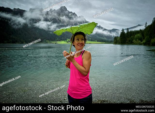 Smiling woman holding green leaf while standing at Haldensee lakeshore during rainy season
