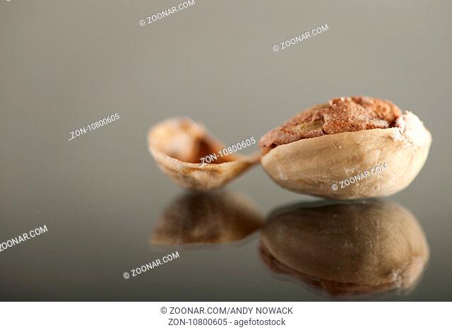 Geöffnete Pistazie auf einer Glasplatte mit daneben liegender Schale. Open pistachio on a glass plate with adjacent shell