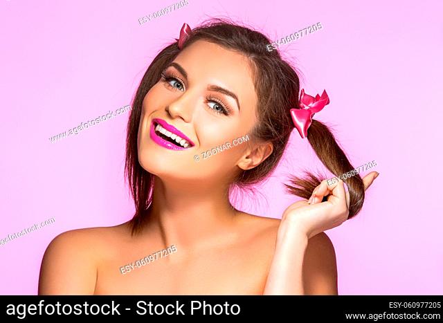 beautiful young woman with pink makeup and two girly ponytails. Beauty shot on pink background. copy space