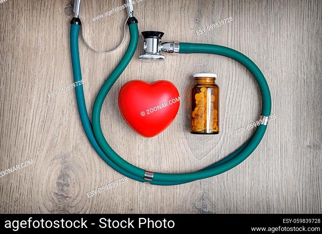 Overhead view of a stethoscope, a glass of pills and a red heart shape