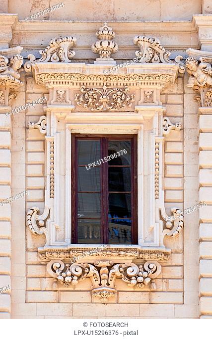Window detail: ornate Baroque facade of Palazzo del Seminario, ornately carved in Leccese style, 8 - paned window, reflection of Duomo and balustrade, Lecce