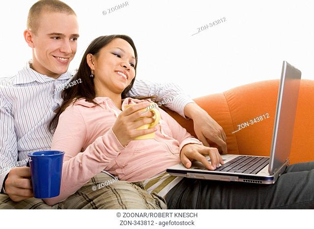 Junges Paar sitzt lachend auf dem Sofa mit Teetassen und Laptop
