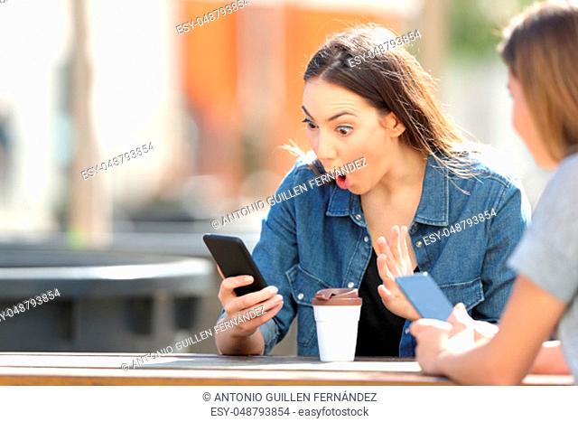Surprised woman checking smart phone online content sitting in a park