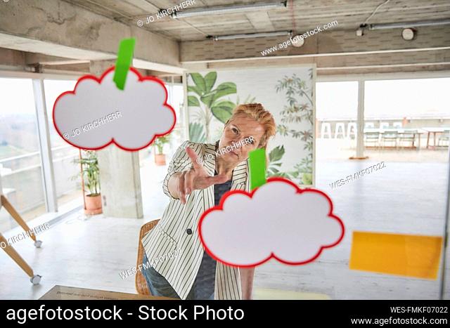 Businesswoman looking at adhesive notes sticked on glass wall while doing business plan at office