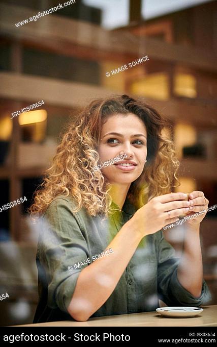 Young woman holding coffee cup behind cafe window