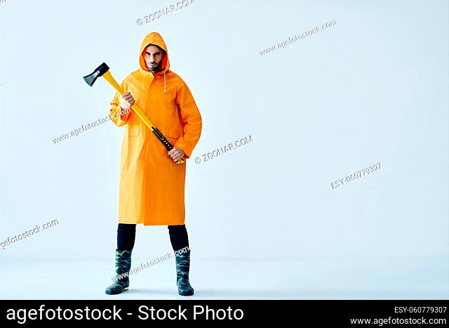 Full length portrait of young handsome man in bright raincoat holding big axe with copy space. Brutal male, lumberjack, fisherman with ax