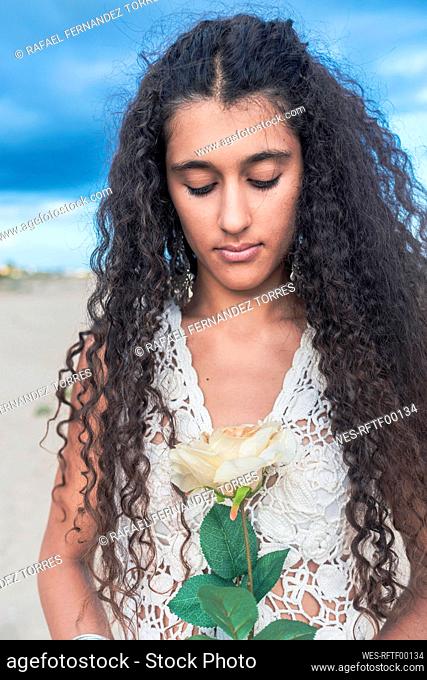 Teenage girl with curly hair holding flower at beach
