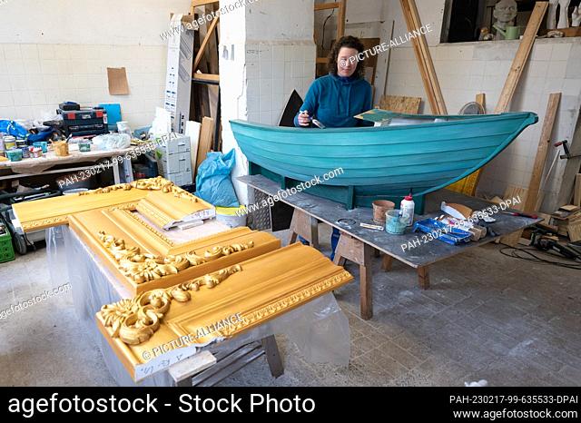 17 February 2023, Saxony, Dresden: Anne Rauschenberg, theater sculptor, works on a wooden boat in a workshop. The boat as well as the frame (l)