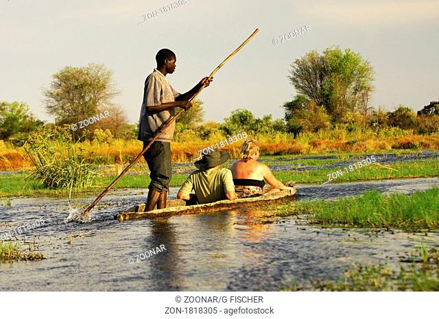Kahnfahrer mit Touristen im traditionellen Mokoro Einbaum auf Exkursion im Okavango Delta, Botswana / Poler with tourists in a tradiional mokoro logboat on...
