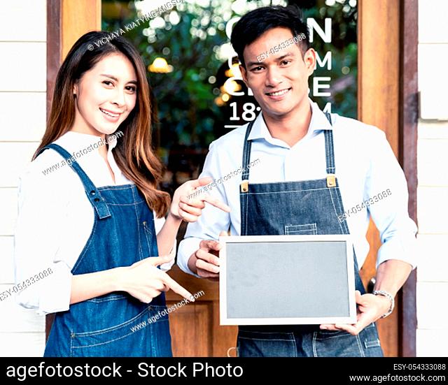Asian young adult owners of Small business cafe holding blank chalkboard in front of coffee retail shop. Using as startup SME concept. Square crop