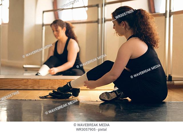 Irish dancer sitting front of mirror on floor tying her shoelace