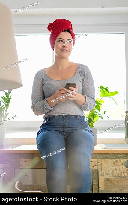 Smiling woman with head wrapped in a towel holding smartphone