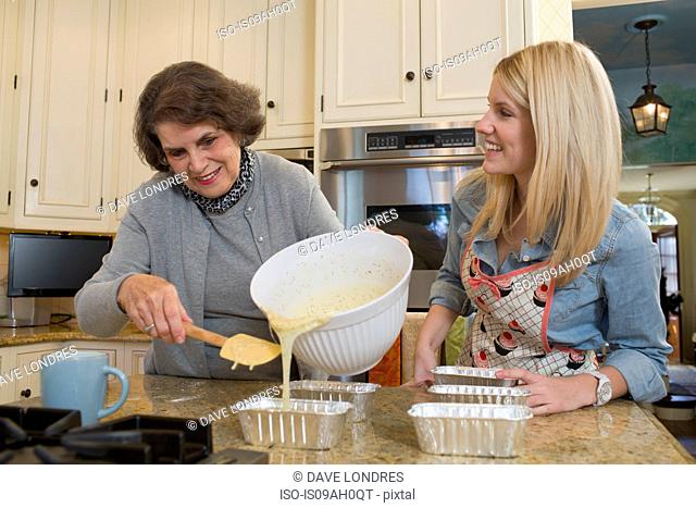 Senior woman and granddaughter pouring mixture into baking tins
