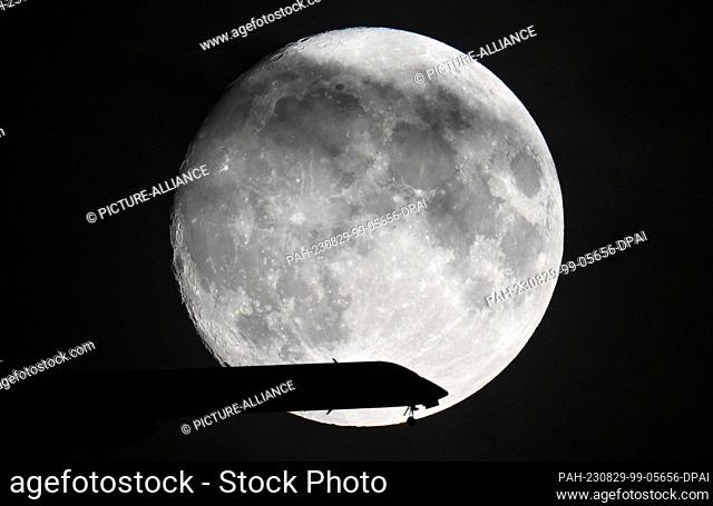 29 August 2023, Hesse, Frankfurt/Main: A passenger plane is on approach to Frankfurt Airport while the moon shines in the evening sky