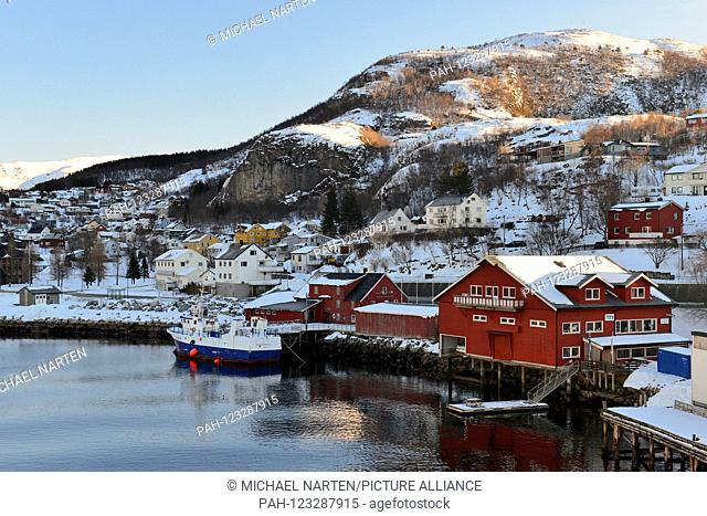 Some buildings from the town Ørnes directly at the waterside by the harbour with sunlight on the snowy mountain in the background