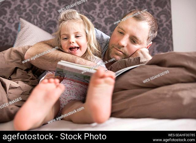 Father and daughter reading a book in bed