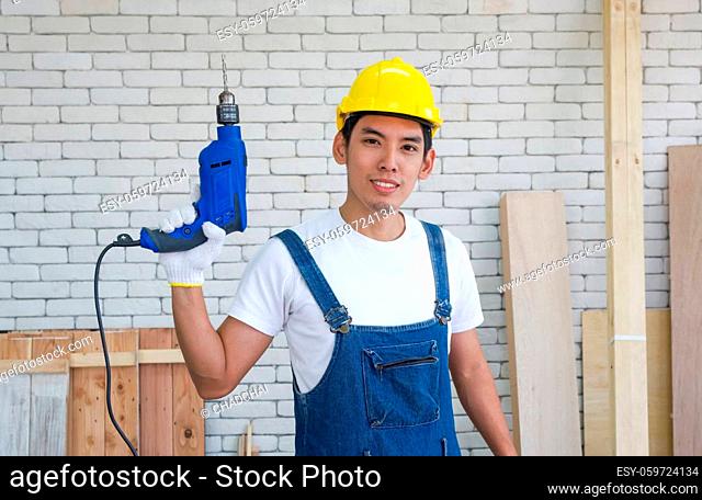 Asian carpenter wearing a yellow hardhat, poses confidently before beginning the job of receiving orders at the wood working place