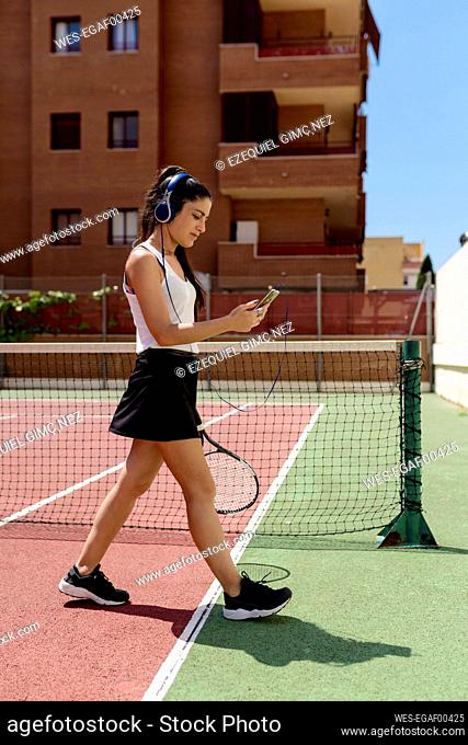 Female tennis player wearing headphones using smart phone while walking in court