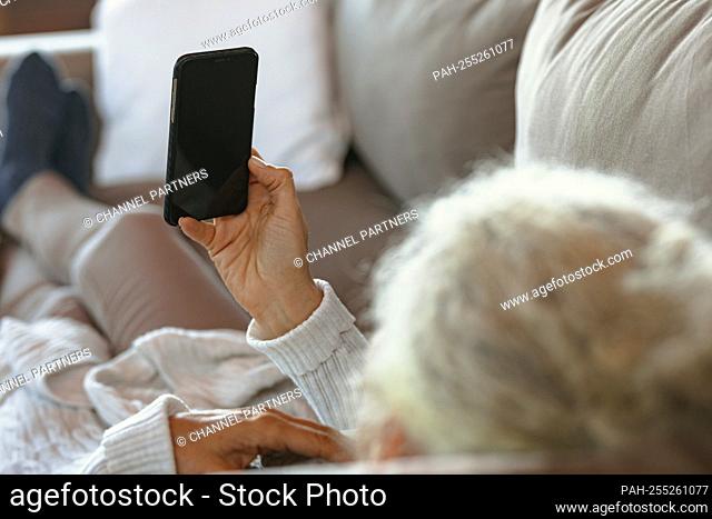 Senior caucasian woman laying and using smartphone in the modern living room. retirement lifestyle, spending time alone at home