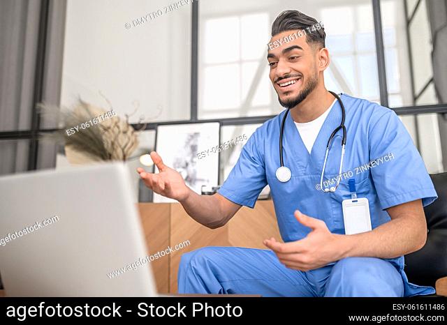 Smiling young male doctor dressed in uniform carrying out a medical consultation over the Internet