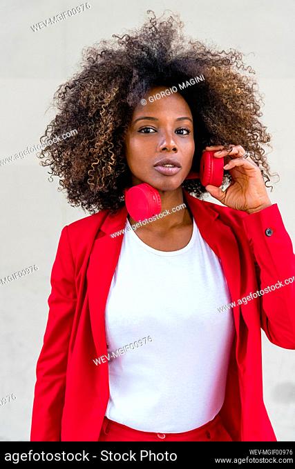 Curly hair woman with headphones standing against wall