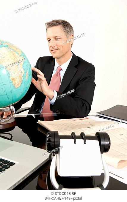 Smiling manager at desk looking at globe