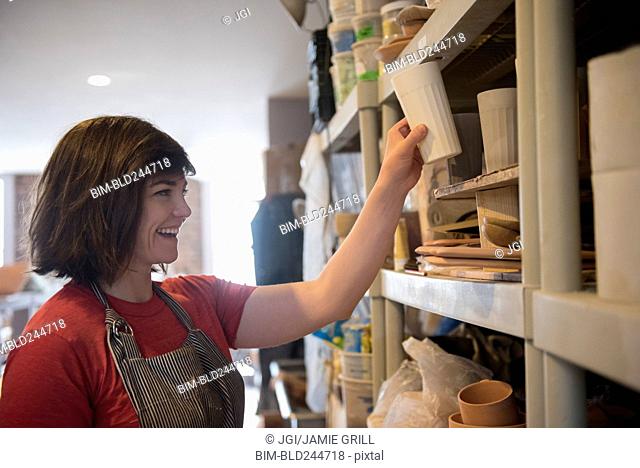 Smiling Caucasian woman placing cup on shelf in workshop