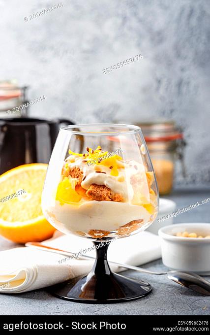 Glass with Healthy homemade layered dessert trifle with orange, biscuit, yogurt and granola