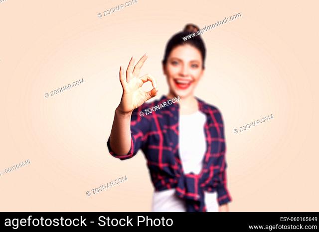 OK. Happy toothy smiley young woman showing OK sign with fingers. studio shot on beige background. focus on hand