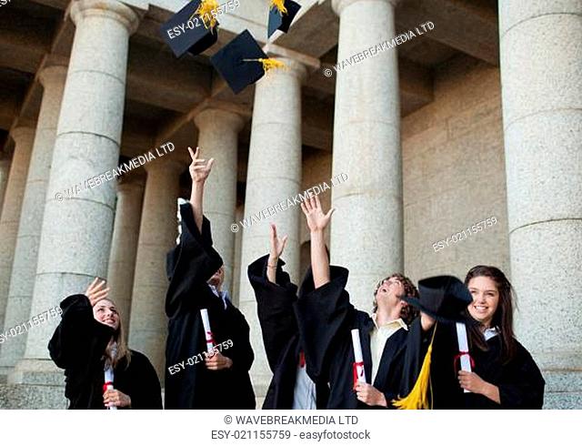 Happy graduates throwing their hats in the sky in front of their university