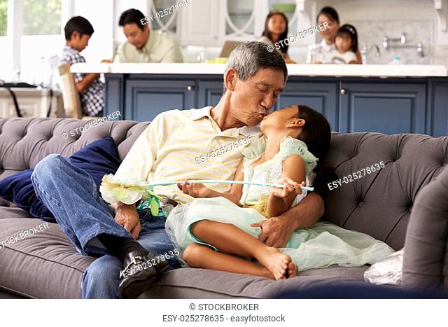 Grandfather And Granddaughter Relaxing On Sofa At Home