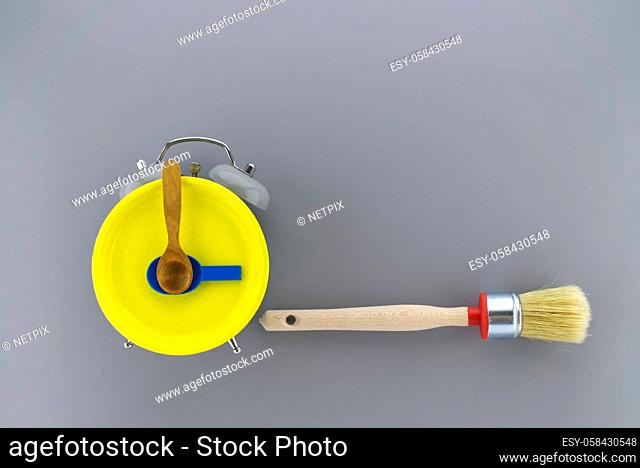 Creative DIY, decorating or renovations background with two clean bristle brushes and a colorful yellow alarm clock with tools for hands forming a border on...