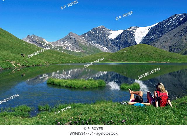 two teens sitting in mountain meadow and enjoying the view to mountain lake, France, Savoie, Sainte-Foy Tarentaise