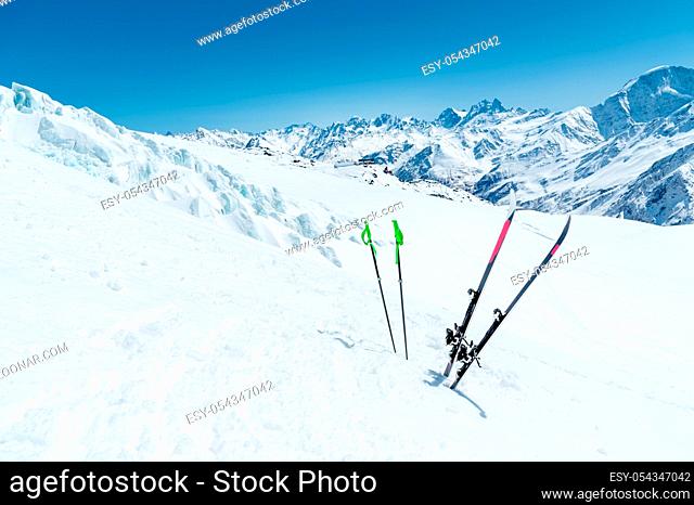 A pair of skis and ski poles stick out in the snow on the mountain slope of the Caucasus against the backdrop of the Caucasian mountain range and the blue sky...
